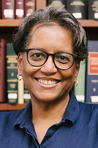 Hon. Phyllis Thompson, head and shoulders, law books in the background, smiling and wearing a blue collared shirt